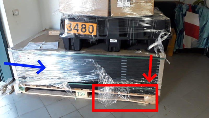 Dettaglio del lato del bancale di legno, rotto e fratturato, con evidente cedimento strutturale sotto il carico della batteria Tesla Powerwall 3.